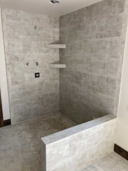 Modern Master Bath Curbless walk-in shower with pebble tile flooring and light gray wall tiles.