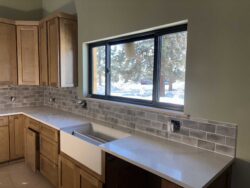 Custom Kitchen Backsplashes Gray glass subway tile kitchen backsplash installed behind a farmhouse sink.