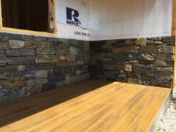 Stone Veneer & Wainscoting Natural stone veneer wainscoting installed on a residential exterior with a wood deck.